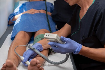 Clinician using Doppler device to assess blood flow for PAD diagnosis in lower leg