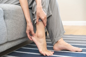 Person sitting on Sofa holding his foot with pain